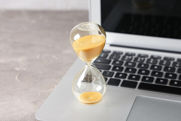 Wall Mural - Stylish hourglass with yellow sand and laptop on table at workplace