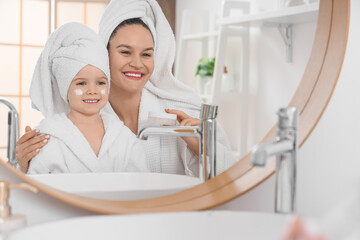 Sticker - Cute little happy girl and her mother in bathrobes with jar of cream near mirror at home