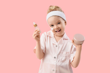 Sticker - Cute little happy girl in pajamas with jar of cream and cosmetic oil on pink background