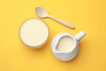 Wall Mural - Tasty condensed milk in bowl and jug with spoon on orange background, top view