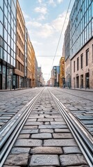 Aufkleber - Low angle view of empty cobblestone street with tram rails in city center, modern buildings lining both sides under a cloudy sky, creating urban perspective