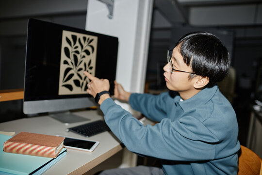 Man examining intricate leaf design on desktop computer screen in office environment, surrounded by book and smartphone