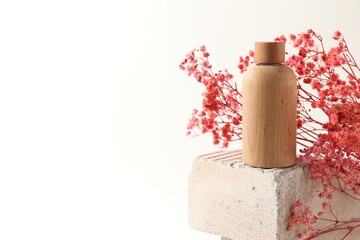 Wall Mural - Bottle of cosmetic product and pink gypsophila flowers on concrete block against white background, space for text