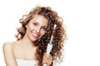 © artmim - Cheerful woman with curly hairstyle using hot curling tongs iron, indoor fashion portrait. Coiffure, beauty salon and hair styling concept