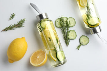 Wall Mural - Lemon water in bottles, rosemary, fresh fruits and slices of cucumber on white background, flat lay