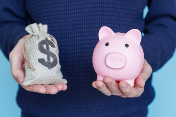 Wall Mural - Retirement savings. The man holds a pink piggy bank in one hand and a bag of money in the other. The concept of financial thrift.