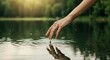 © Outkast - Serene hand reaching into calm lake water, creating ripples amidst lush greenery and soft sunlight