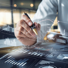 Poster - A close-up shot of a personâ€™s hand holding a pen while interacting with digital financial data and analytics, symbolizing business analysis, technology, and data-driven decision-making.