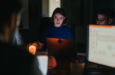 Wall Mural - A group of business coworkers engaged in a focused meeting, collaborating on laptops late at night. The dimly lit office setting emphasizes their dedication and teamwork to meet deadlines and goals.