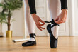 © Юлия Завалишина - Ballerina puts on pointe shoes on leg in dance class. Classical ballet dancer woman in dance studio. Ballerina putting on tying classical pointe shoes for dance training. Ballet school concept
