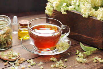 Wall Mural - Linden herbal tea in a glass cup with flowers on wooden rustic background, closeup, sleep and relax drink, natural medicine and naturopathy concept