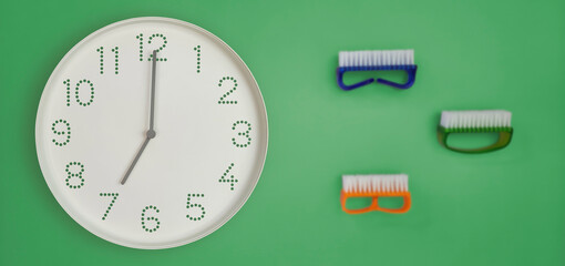 Banner with wall clock on green background with colorful brushes for dishes. household cleaning supplies and clock at 7 o'clock morning, beginning of the day