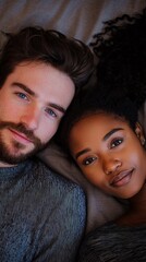 Aufkleber - A white man and a black woman lie closely together on soft bedding, their serene gazes inviting warmth and intimacy in a cozy atmosphere. Time seems to stand still as they embrace the moment