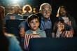© Marko Geber - Grandfather with grandchildren watching movie in cinema with popcorn