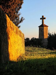Poster - Historical stone cross silhouetted against a warm sunset with lush green grass : Generative AI