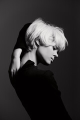 Wall Mural - Elegant woman with short blonde hair posing gracefully against a dark background, showcasing modern hairstyle and fashion, expressing serenity and confidence.