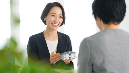 Aufkleber - 女性、ビジネス、ビジネスウーマン、ミーティング、打ち合わせ、商談、説明、住宅、提案、接客、不動産、相談、会話、笑顔、日本人、設計、営業、メーカー、模型、マイホーム、販売、取引、モデルハウス、オフィス、おすすめ、事務所、賃貸、新築、リフォーム、設計士、建築士、建築、仕事、働く、アドバイザー、住まい、受付、窓口、ビジネスパーソン、ミドル、スーツ、会議、面談、建物、会社、案内、紹介、マンション、インテリ