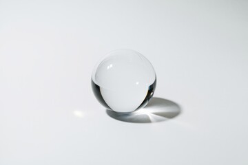 Poster - A clear glass sphere casts a shadow on a white background, showcasing its reflective properties.