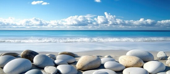 Poster - Calm shoreline with smooth grey pebbles and serene blue ocean under a clear sky with fluffy white clouds