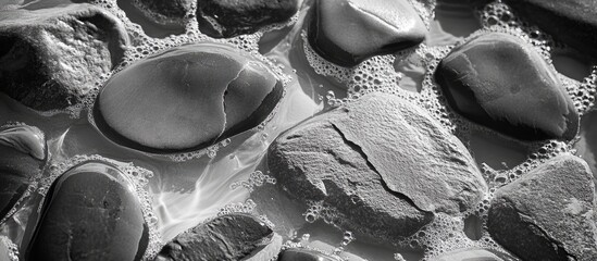 Aufkleber - Rocky beach closeup in black and white featuring smooth stones and gentle waves splashing over the surface creating a serene coastal atmosphere