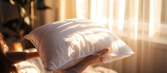 Sticker - Cozy morning light illuminating a hand holding a fluffy pillow comforter with soft shadows and text space in a warm atmosphere