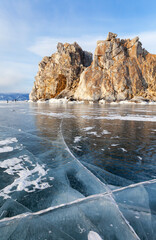 Wall Mural - Frozen Lake Baikal on sunny cold winter day. View of natural landmark of Olkhon Island - famous Shamanka Rock or Cape Burkhan from blue  ice with cracks. Popular tourist destination. Scenic landscape