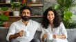 © Ilja - Happy Indian Couple Relaxing on Sofa, Enjoying Morning Coffee Together in their Cozy Living Room