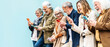 © Davide Angelini - Group of senior people using technology devices together standing on a blue wall - Happy older friends having fun watching funny video on smartphone - Tech and modern elderly concept
