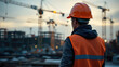 © O - Young caucasian man in construction gear overseeing busy urban building site at dusk