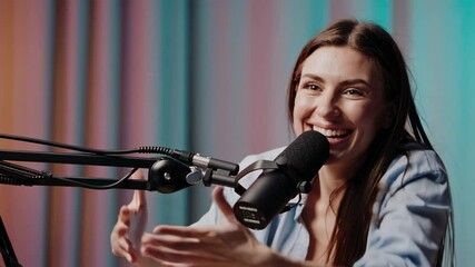 Poster - Content creator woman records a podcast, laughing and gesturing while speaking into a microphone in a colorful studio, shown in slow motion