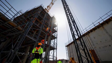 Poster - Construction workers in safety vests and helmets coordinate on a building site, with a crane and scaffolding visible against a sunny sky, captured in a slow motion multi screen composition