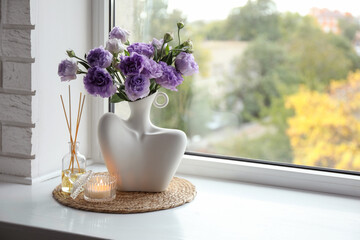 Wall Mural - Stylish vase with beautiful flowers, candle and reed diffuser near window at home, space for text