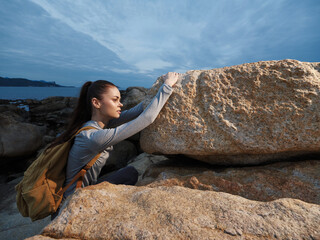 young female climber wearing gray sportswear with a backpack overcoming a rock formation by the sea 