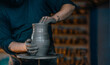 © adrianad - A skilled artisan molds clay on a pottery wheel, focusing intently on shaping a vase with hands covered in wet clay in a workshop setting.