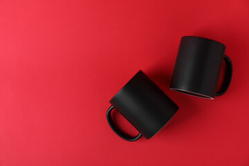 Wall Mural - Two blank black mugs on red background, top view. Mockup for design