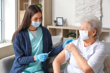 Wall Mural - Young nurse vaccinating senior woman at home