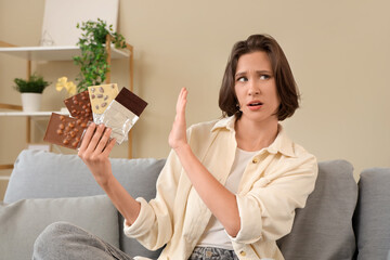 Poster - Beautiful young shocked woman with different tasty chocolate bars sitting on sofa at home