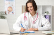 © Pixel-Shot - Beautiful female doctor with modern laptop and clipboard at table in clinic