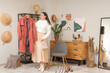 © Pixel-Shot - Young woman with stylish coat near clothes rack at home