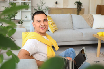 Wall Mural - Young man using laptop near sofa at home