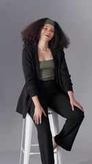 Poster - Photoshoot, fashion and woman on chair, stylish clothes and confident girl on gray studio background. Pose, person and model with trendy outfit, photography and pride with picture and creativity