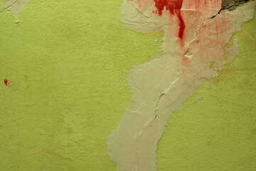 Green damaged plaster on concrete wall, old plaster needs repair. Abstract red paint strokes on wall background, close-up, copy space