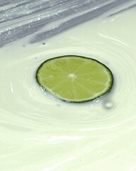Poster - Zesty Lime Slice Floating in Creamy Mixture on a Smooth Surface