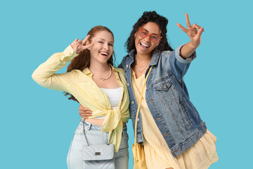 Wall Mural - Beautiful young happy female friends showing victory gesture on blue background