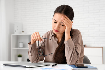 Wall Mural - Tired young Asian businesswoman with headache sitting at her workspace in office