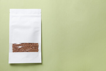 Wall Mural - Paper pouch bag with buckwheat on green background, top view. Space for text