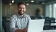 © Viktor - Man sits at desk with laptop. Guy portrait at office workspace, smiles confidently. Pro businessman is happy working on modern computer. Positive work environment.