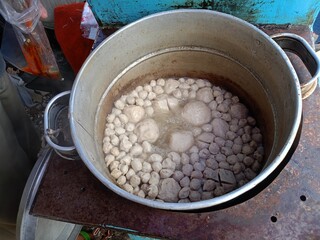 large pot contains meatballs of various sizes that are being boiled in boiling water. The photo was taken from a top angle, showing the atmosphere of a street vendor with simple cooking equipment