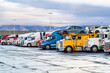 © vit - Industrial grade big rig professional semi trucks tractors with loaded semi trailers standing in row on truck stop parking lot at early morning time ready to go according to the route schedule