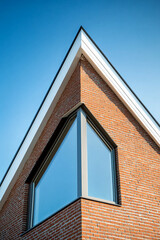 Aufkleber - Close-up of a modern brick house with a large triangular window, showcasing a clean architectural design and geometric patterns against a clear blue sky.